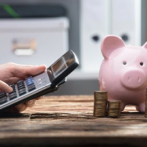 Hands operate pocket calculator near piggy bank