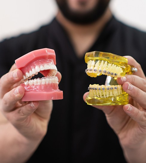 a dental assistant holding a model of a mouth with braces and another with clear aligners