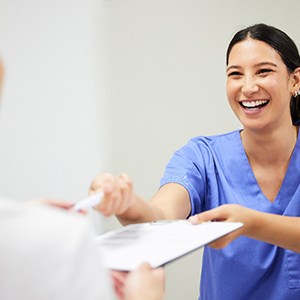 Smiling dental assistant handing patient form
