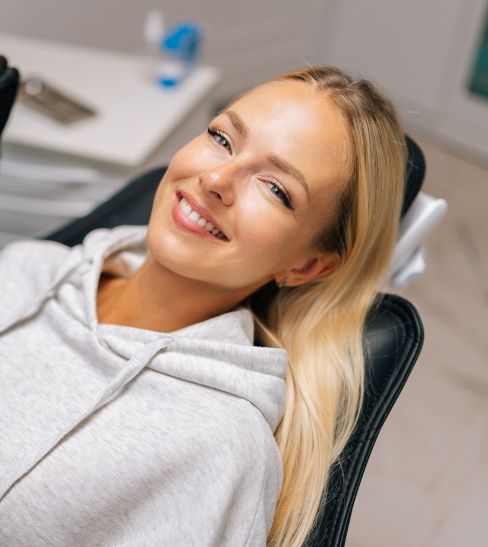 Female patient in hoodie smiling while lying back in dental chair