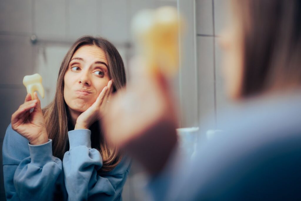 A woman holding a model of a tooth and clutching her jaw in pain